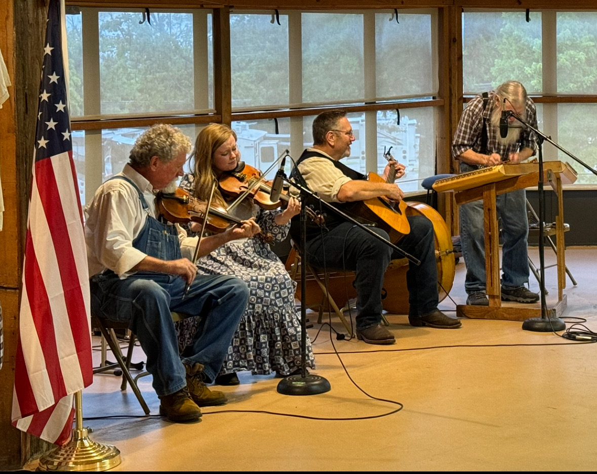 A group of five people are sitting on chairs, playing musical instruments